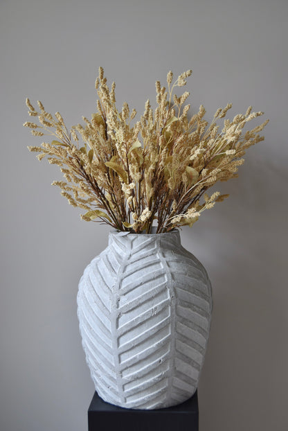 Dried-look grain sorghum spray displayed in a stone chevron style vase placed on a black pedestal.