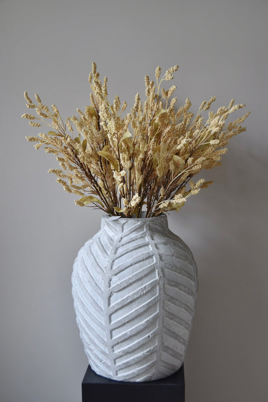 Dried-look grain sorghum spray displayed in a stone chevron style vase placed on a black pedestal.