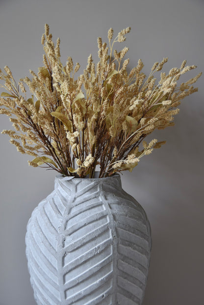 Dried-look grain sorghum spray displayed in a stone chevron style vase placed on a black pedestal.