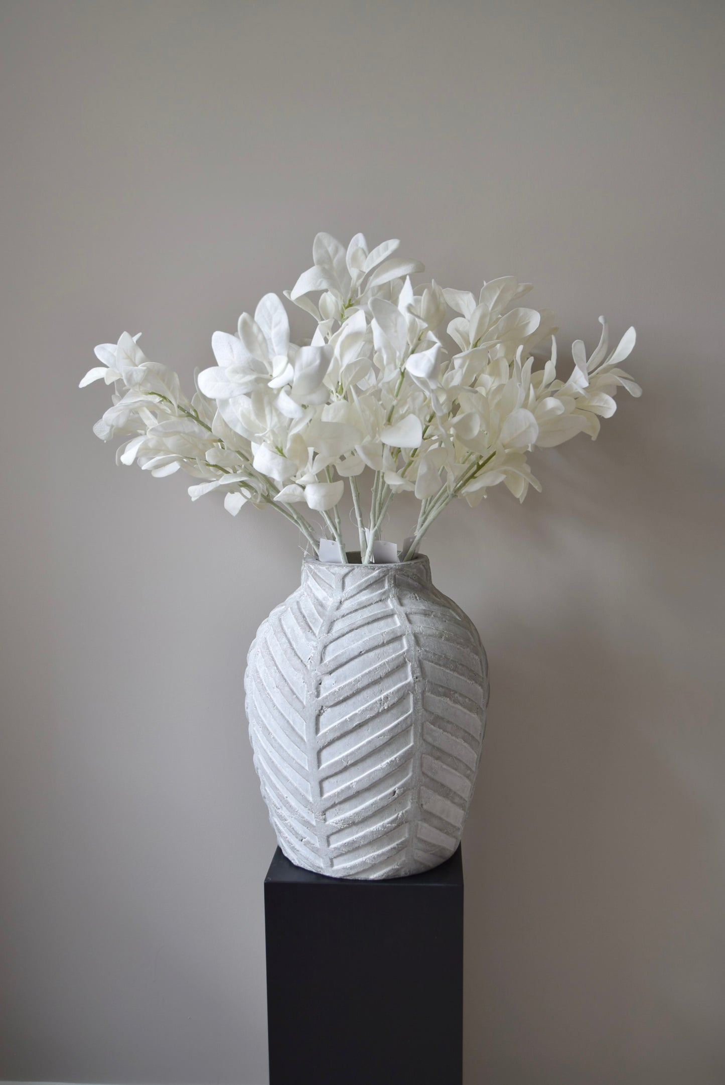 White lamb's ear stem displayed in a chevron stone vase placed on a black pedestal.