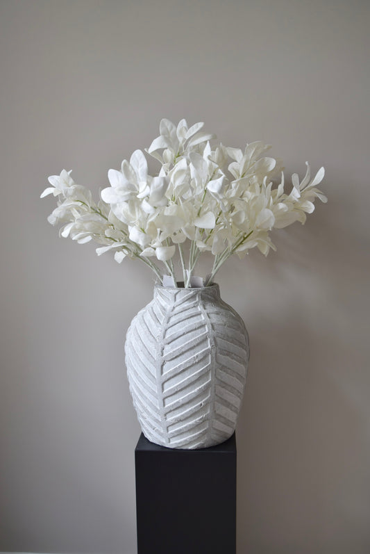 White lamb's ear stem displayed in a chevron stone vase placed on a black pedestal.
