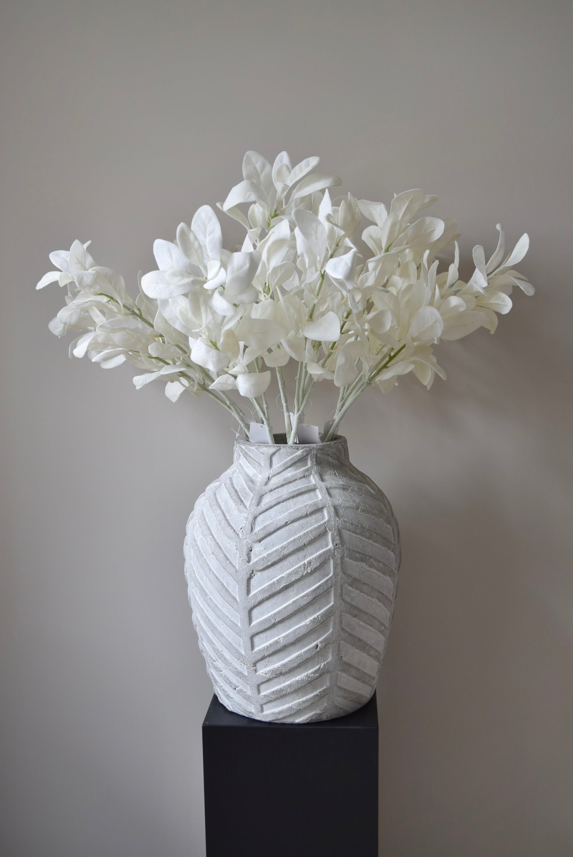 White lamb's ear stem displayed in a chevron stone vase placed on a black pedestal.