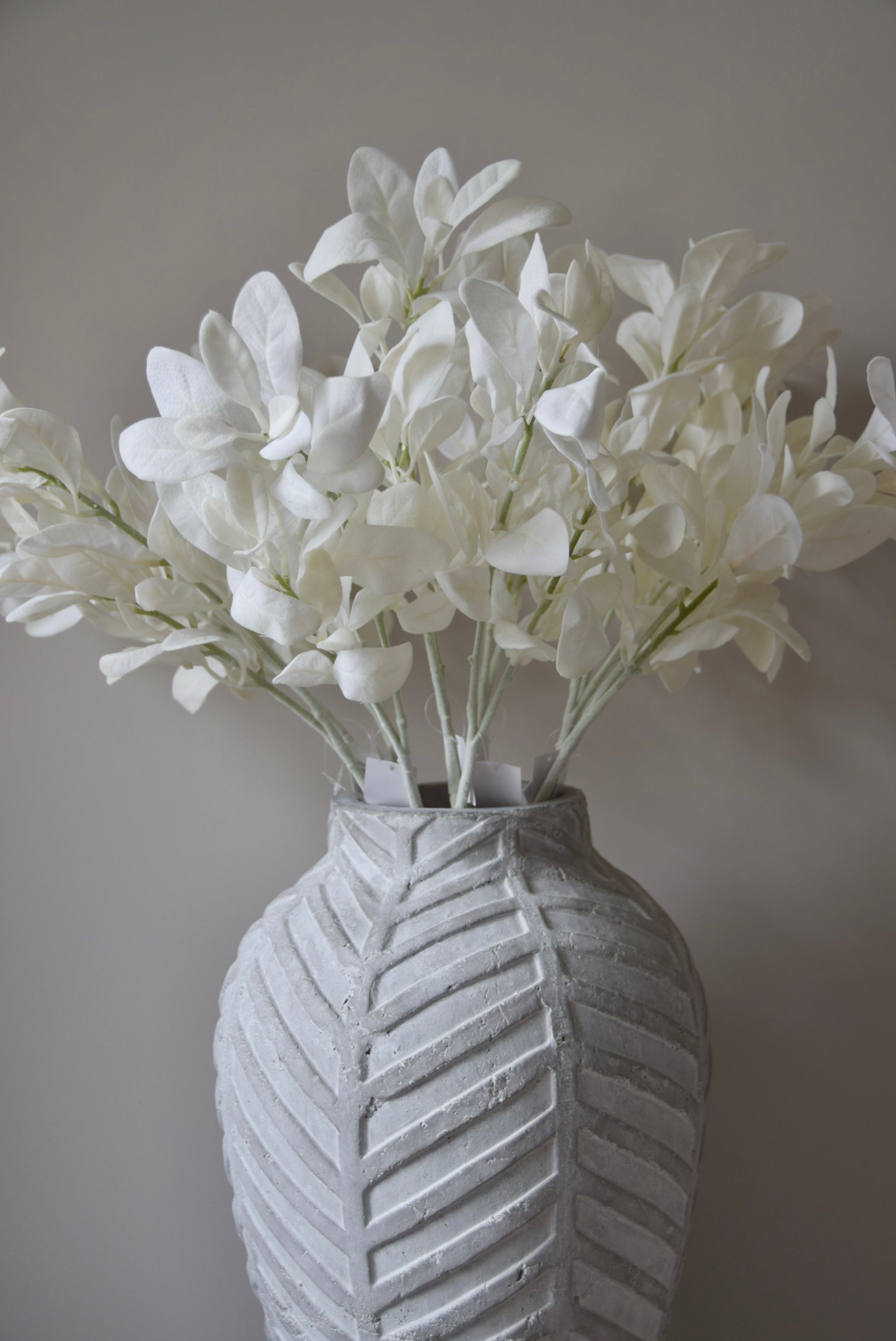 White lamb's ear stem displayed in a chevron stone vase placed on a black pedestal.
