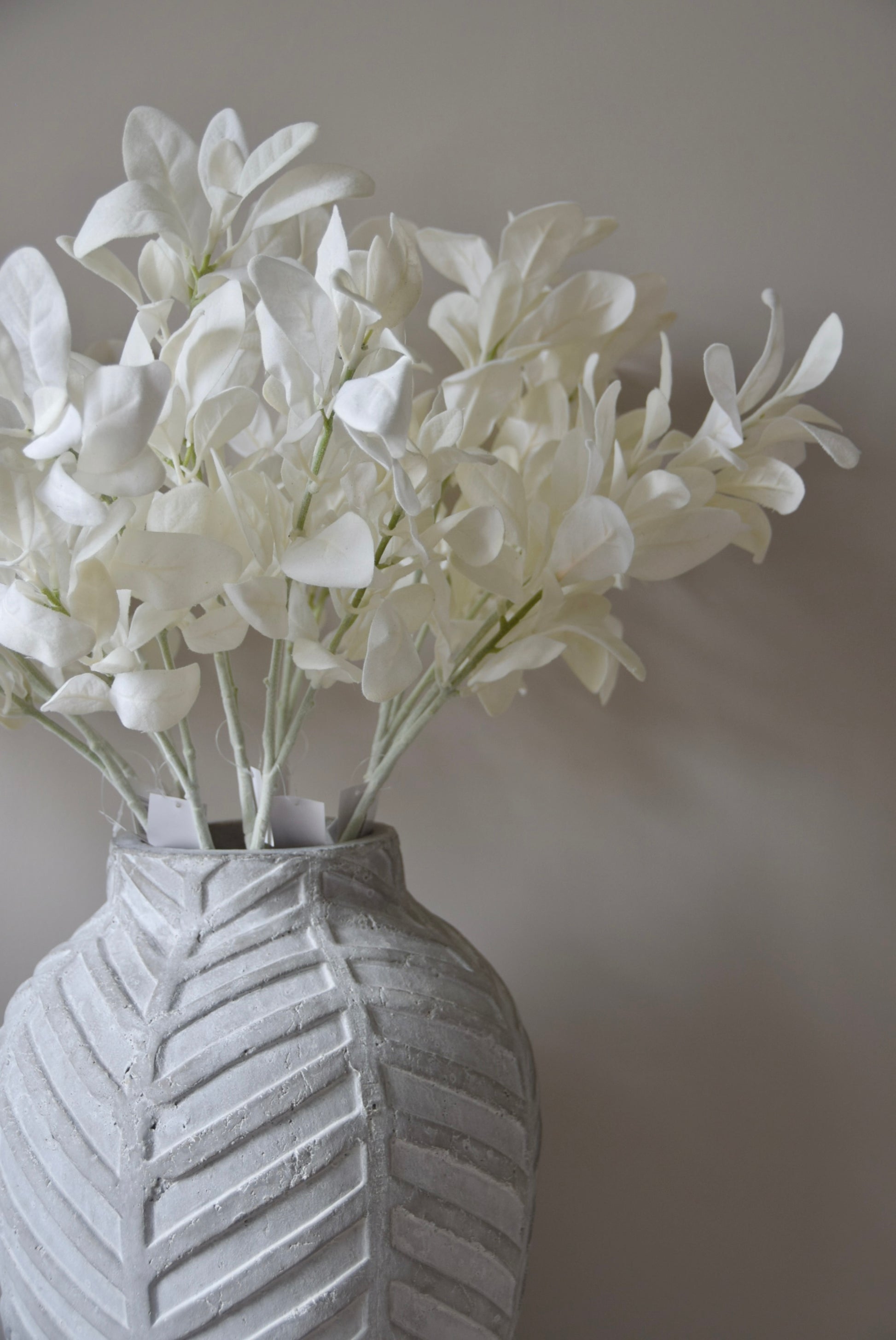 White lamb's ear stem displayed in a chevron stone vase placed on a black pedestal.