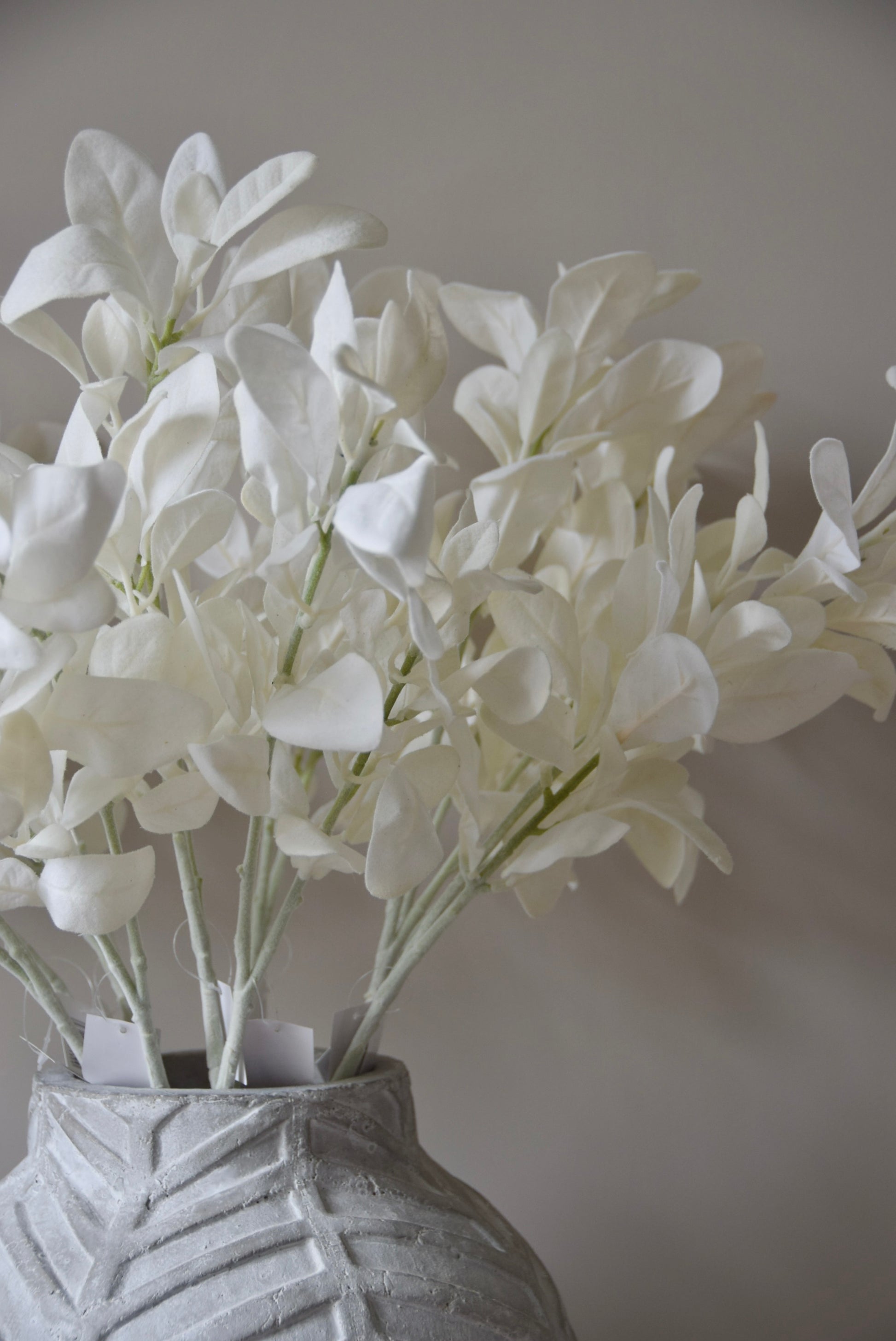 White lamb's ear stem displayed in a chevron stone vase placed on a black pedestal.