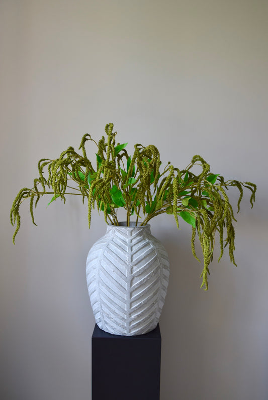 Stone chevron vase placed on a black pedestal displaying a bunch of artificial green catkin stems.
