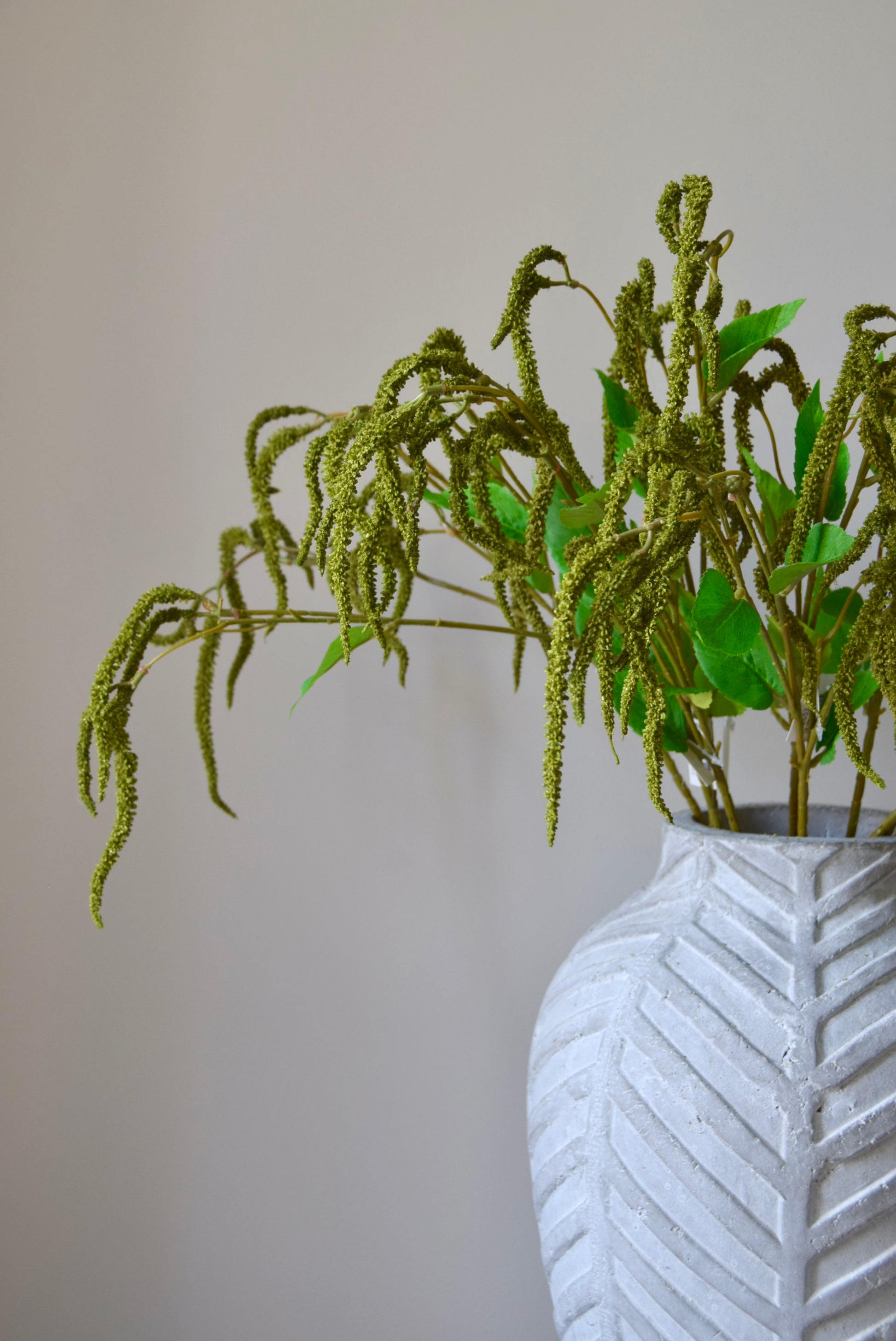 Stone chevron vase placed on a black pedestal displaying a bunch of artificial green catkin stems.