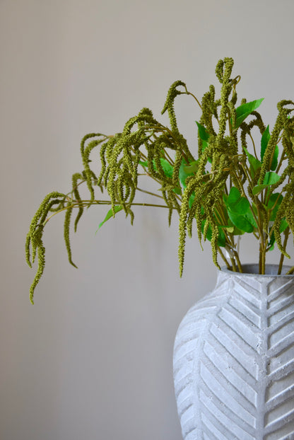 Stone chevron vase placed on a black pedestal displaying a bunch of artificial green catkin stems.