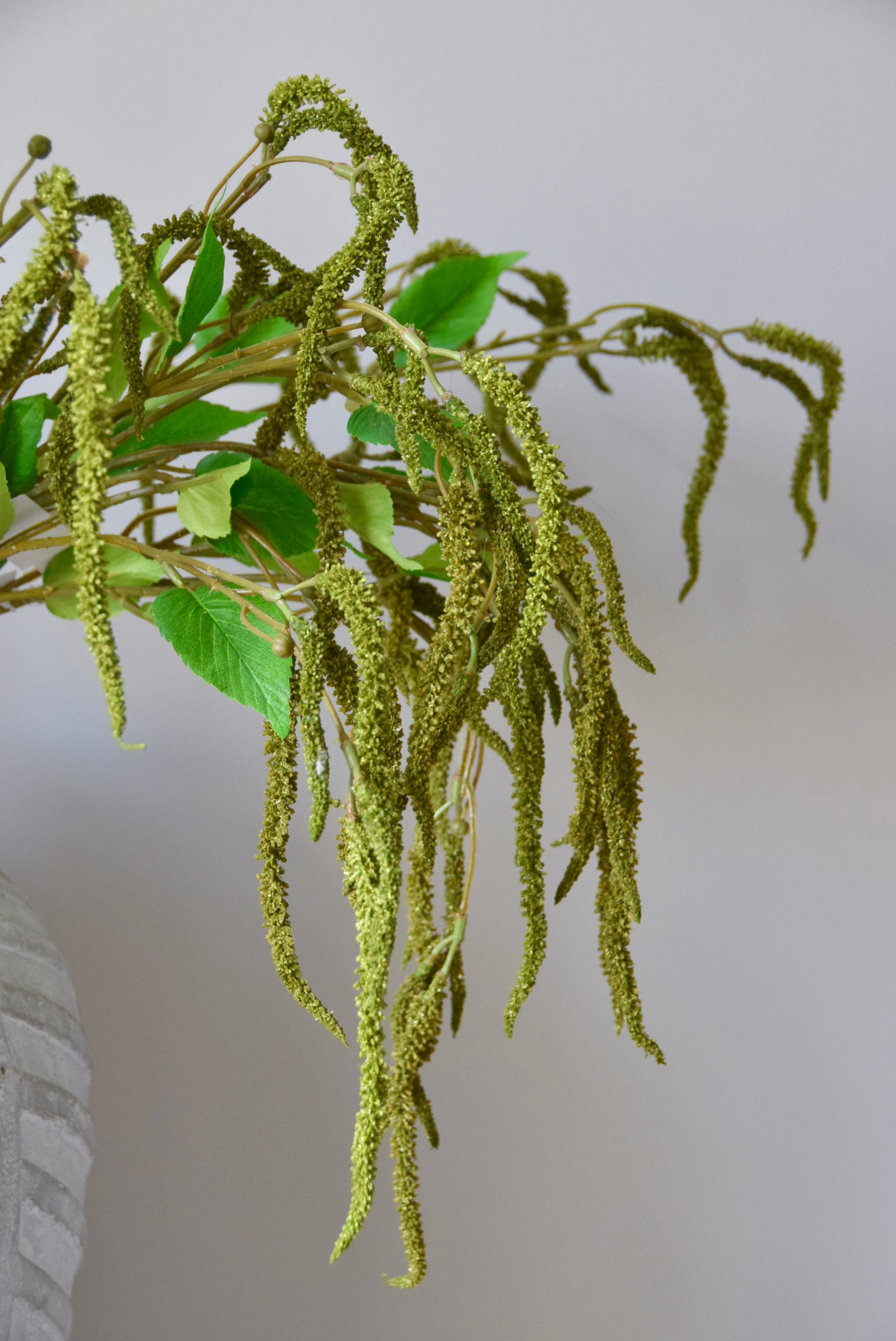 Stone chevron vase placed on a black pedestal displaying a bunch of artificial green catkin stems.