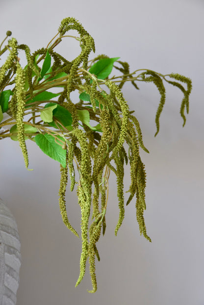 Stone chevron vase placed on a black pedestal displaying a bunch of artificial green catkin stems.