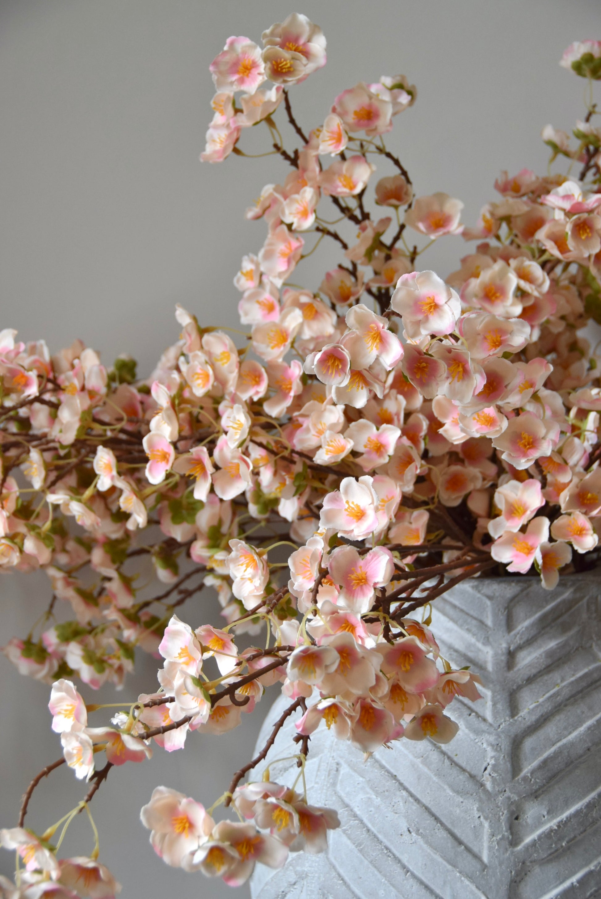 Stone chevron style vase placed on a black pedestal with a bunch of drooping pink plum blossom stems.