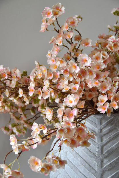 Stone chevron style vase placed on a black pedestal with a bunch of drooping pink plum blossom stems.