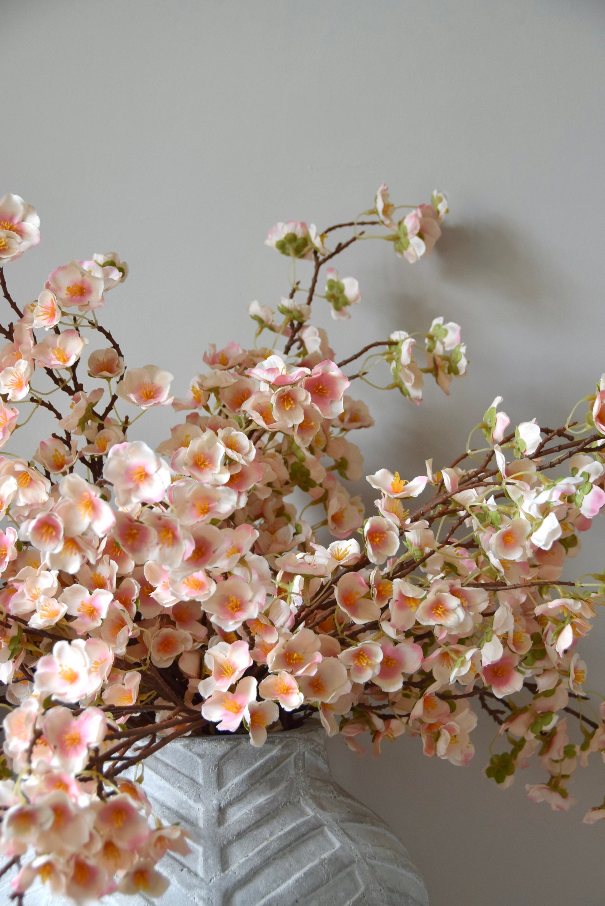 Stone chevron style vase placed on a black pedestal with a bunch of drooping pink plum blossom stems.