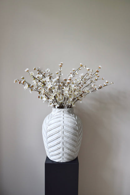 Stone chevron style vase placed on a black pedestal displaying a bunch of artificial cherry blossom branches.