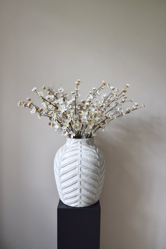 Stone chevron style vase placed on a black pedestal displaying a bunch of artificial cherry blossom branches.