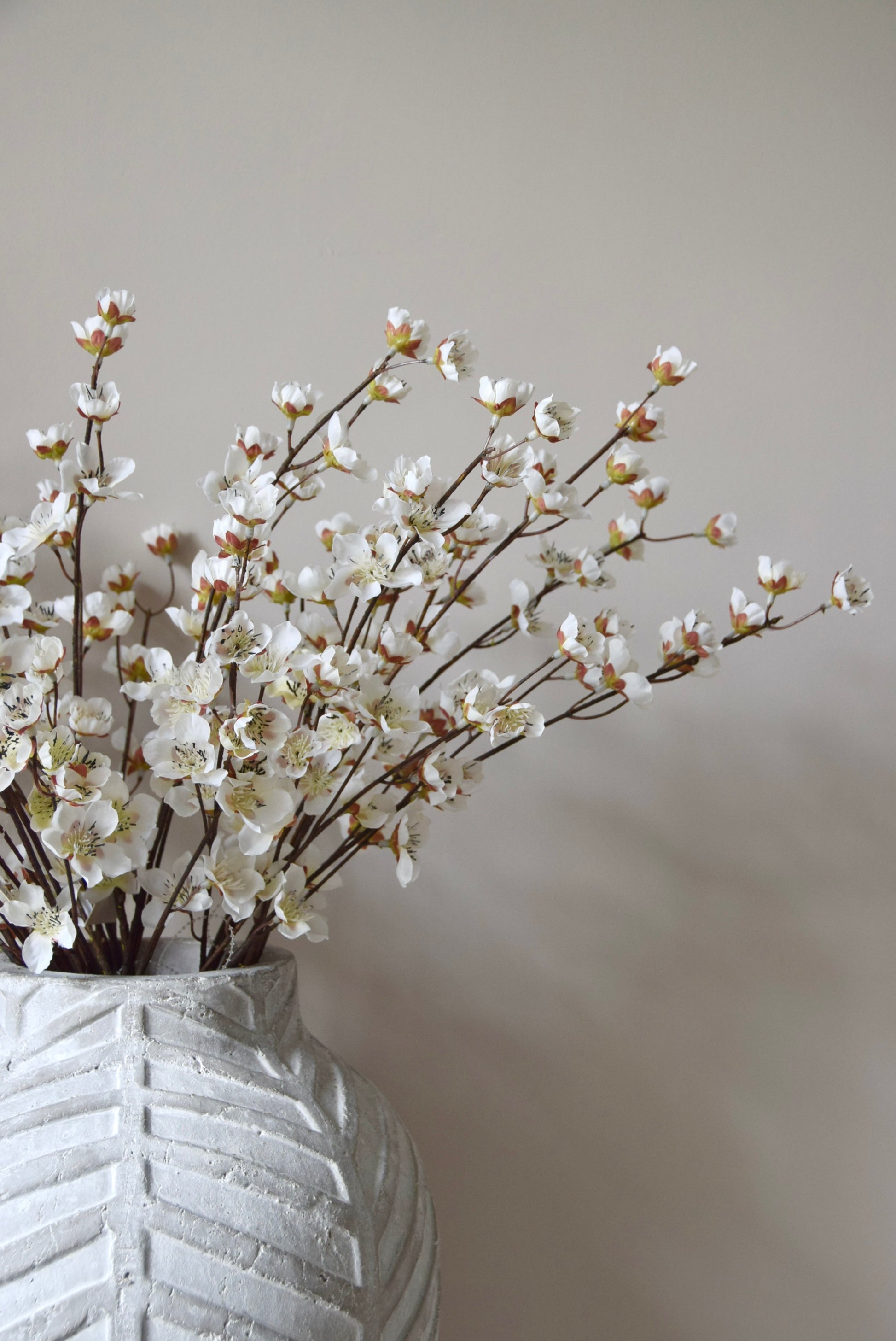 Stone chevron style vase placed on a black pedestal displaying a bunch of artificial cherry blossom branches.