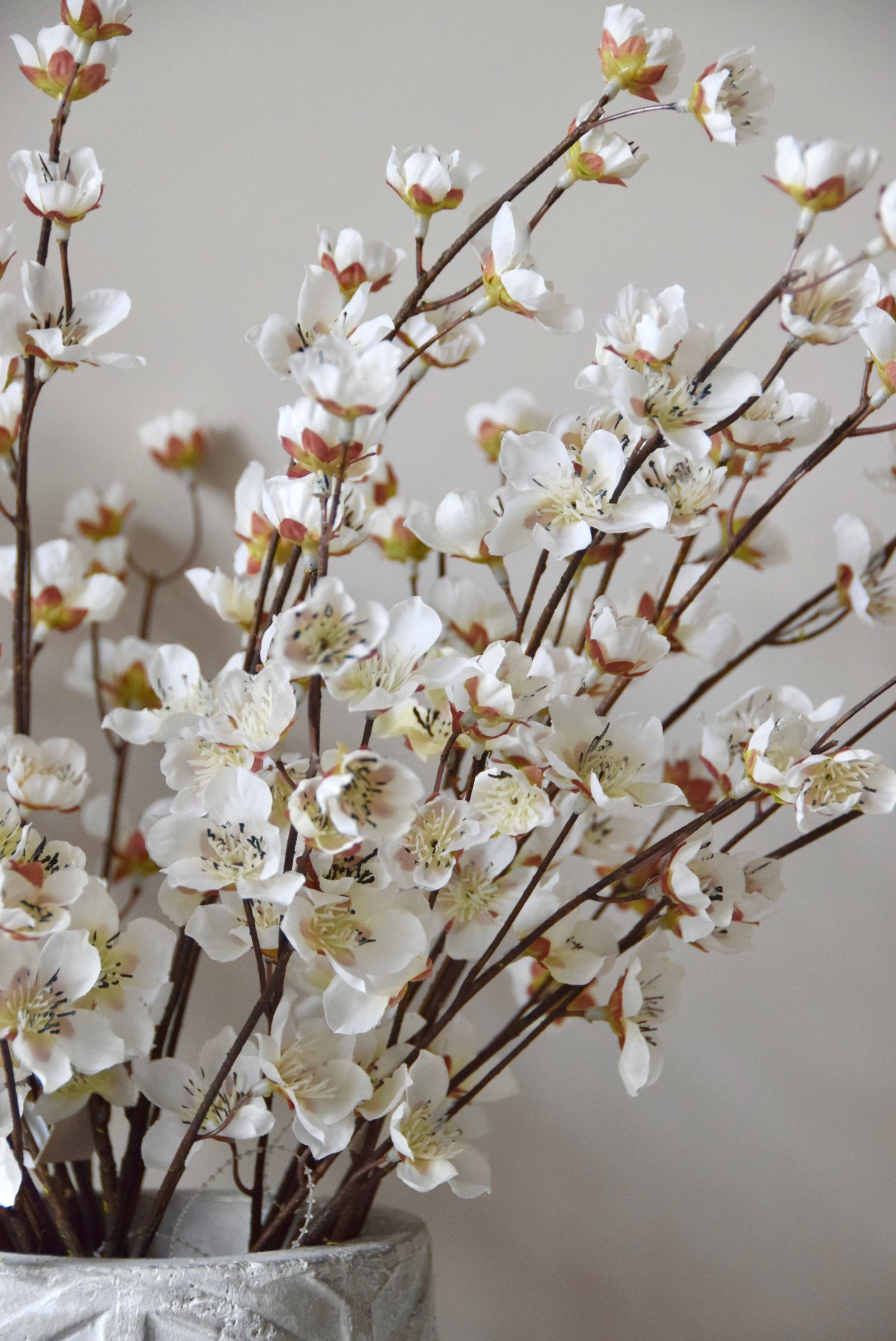 Stone chevron style vase placed on a black pedestal displaying a bunch of artificial cherry blossom branches.