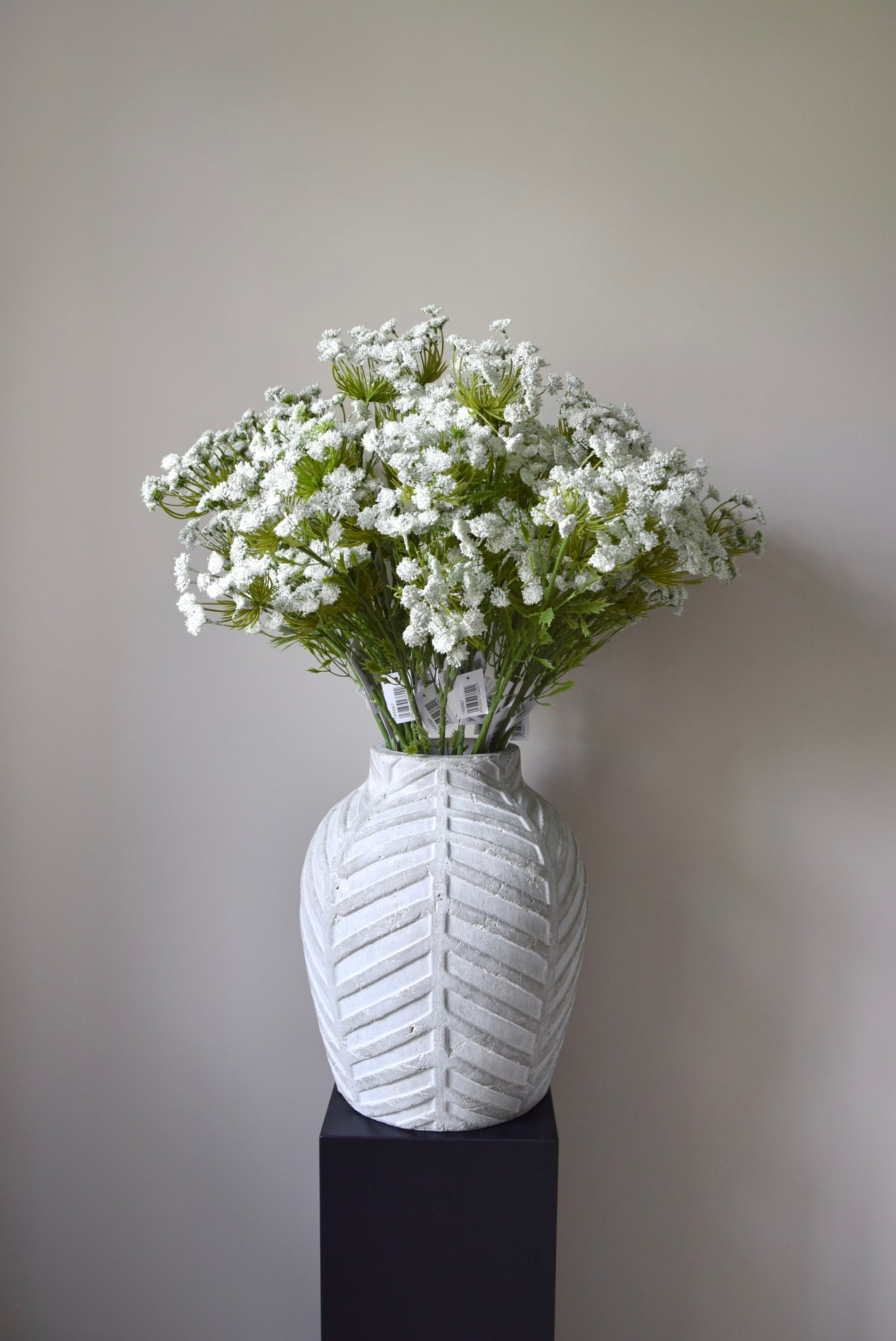 Stone chevron style vase placed on a black pedestal displaying a bunch of white cow parsley.