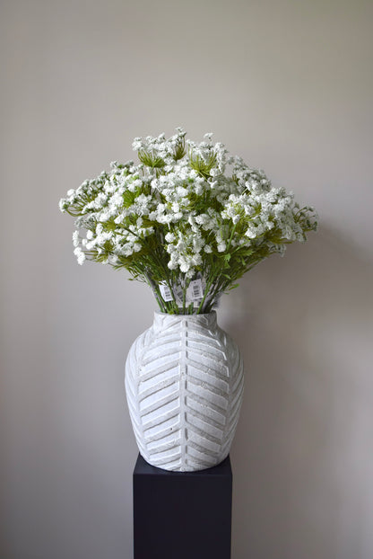Stone chevron style vase placed on a black pedestal displaying a bunch of white cow parsley.