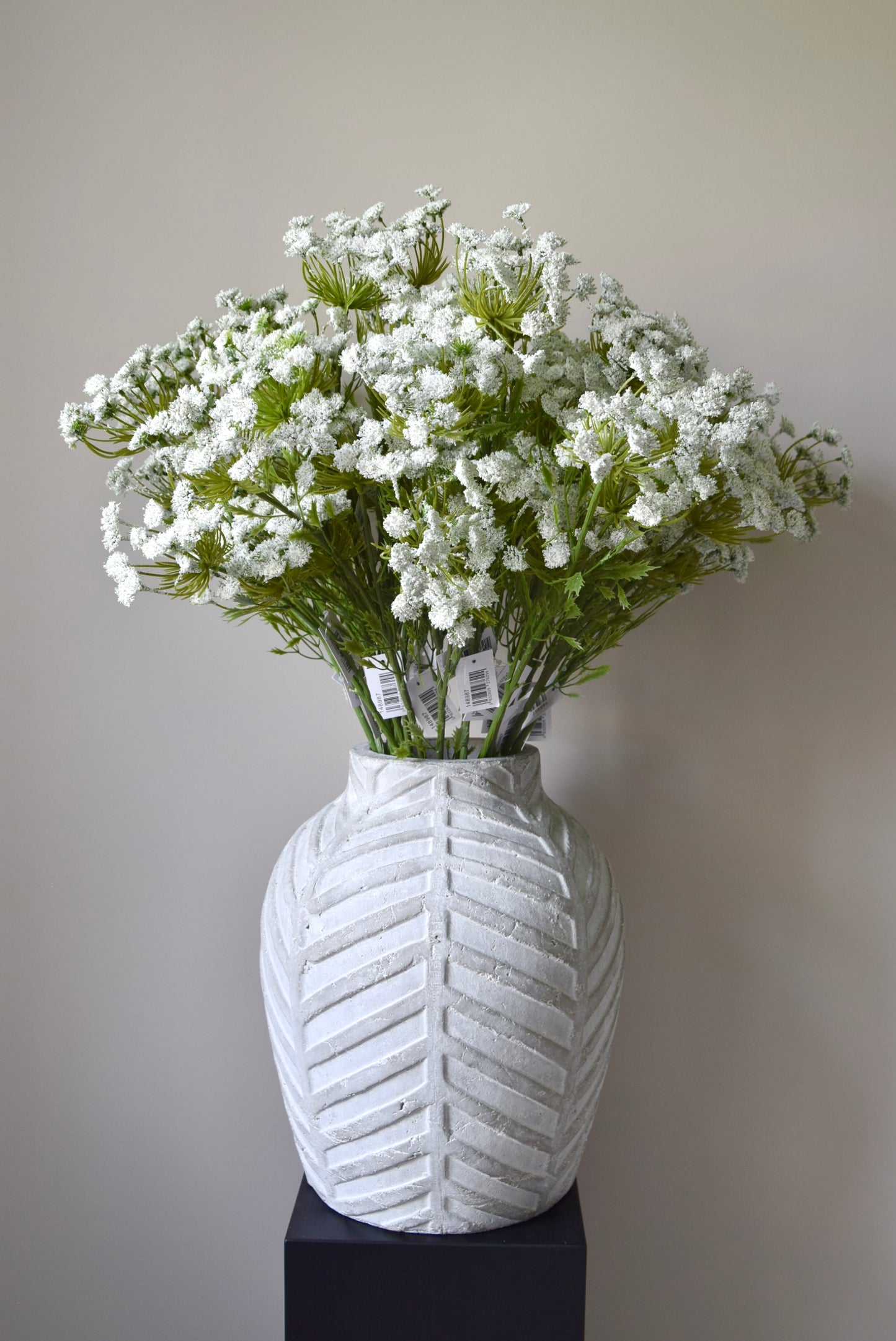 Stone chevron style vase placed on a black pedestal displaying a bunch of white cow parsley.