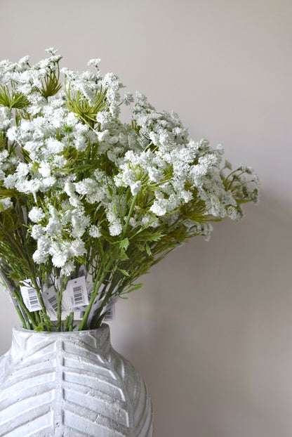 Stone chevron style vase placed on a black pedestal displaying a bunch of white cow parsley.