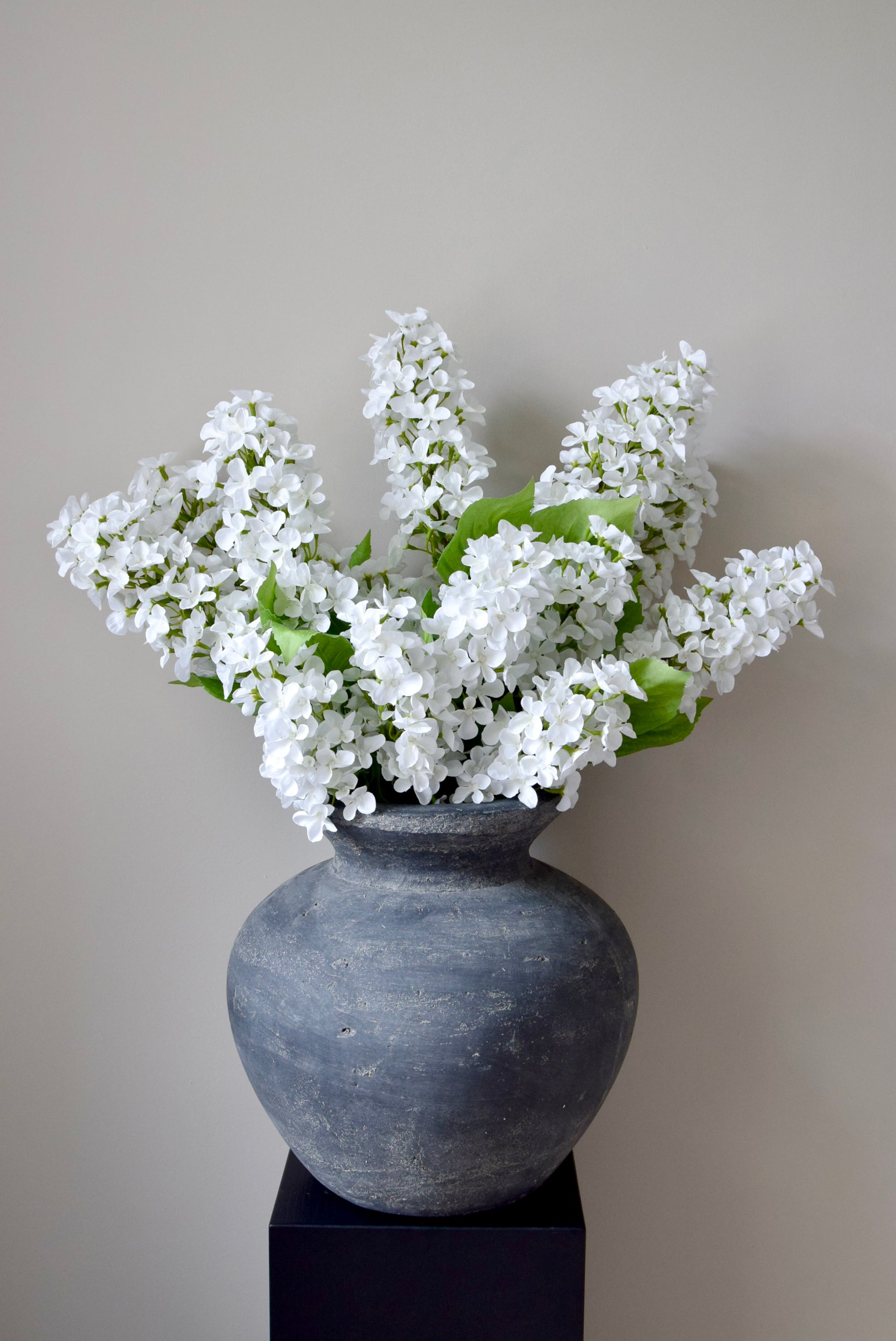 Gray vase with white flowers on a black stand against a plain background