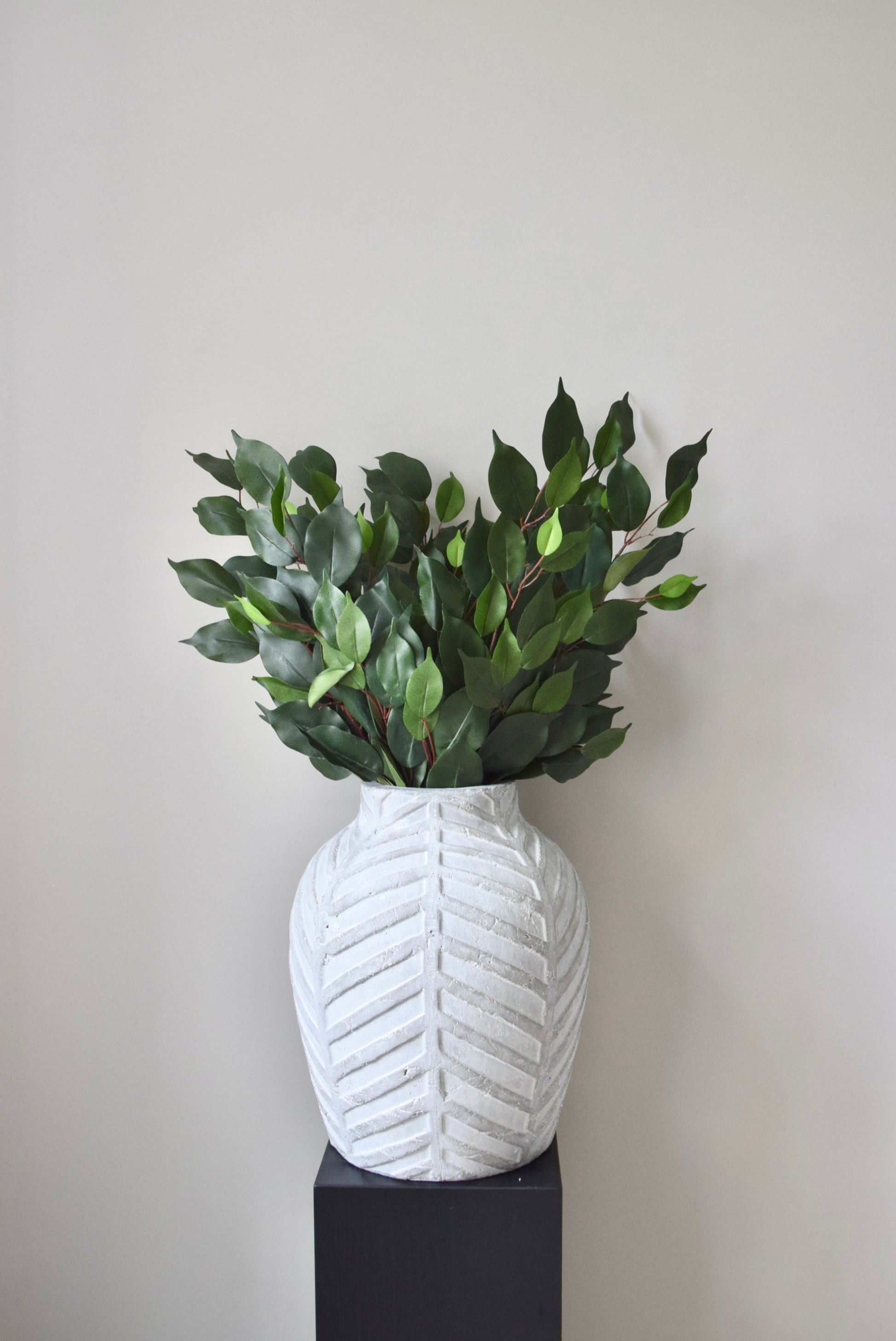 White textured vase with green leaves against a plain background