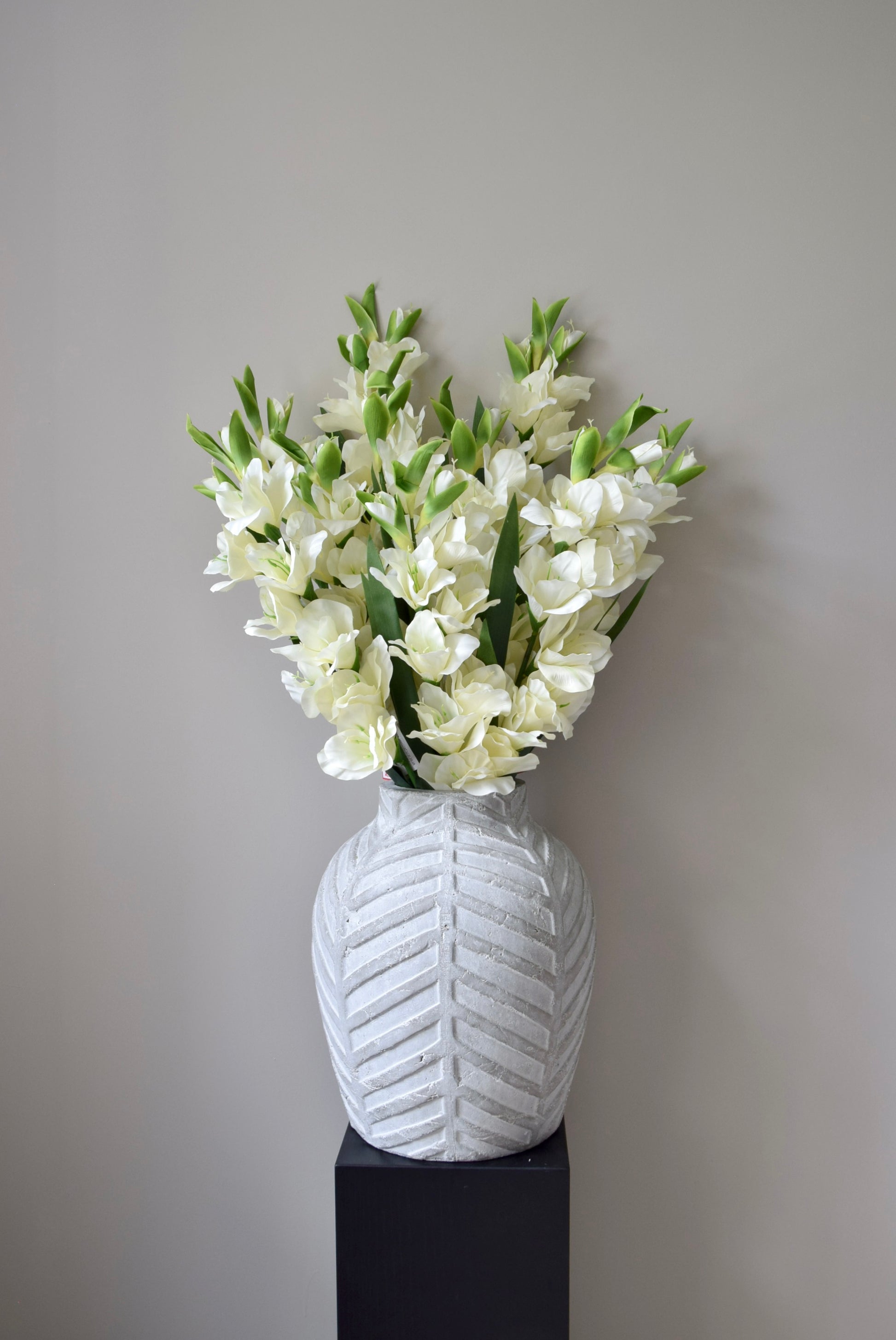 White vase with a textured pattern containing white flowers against a plain background