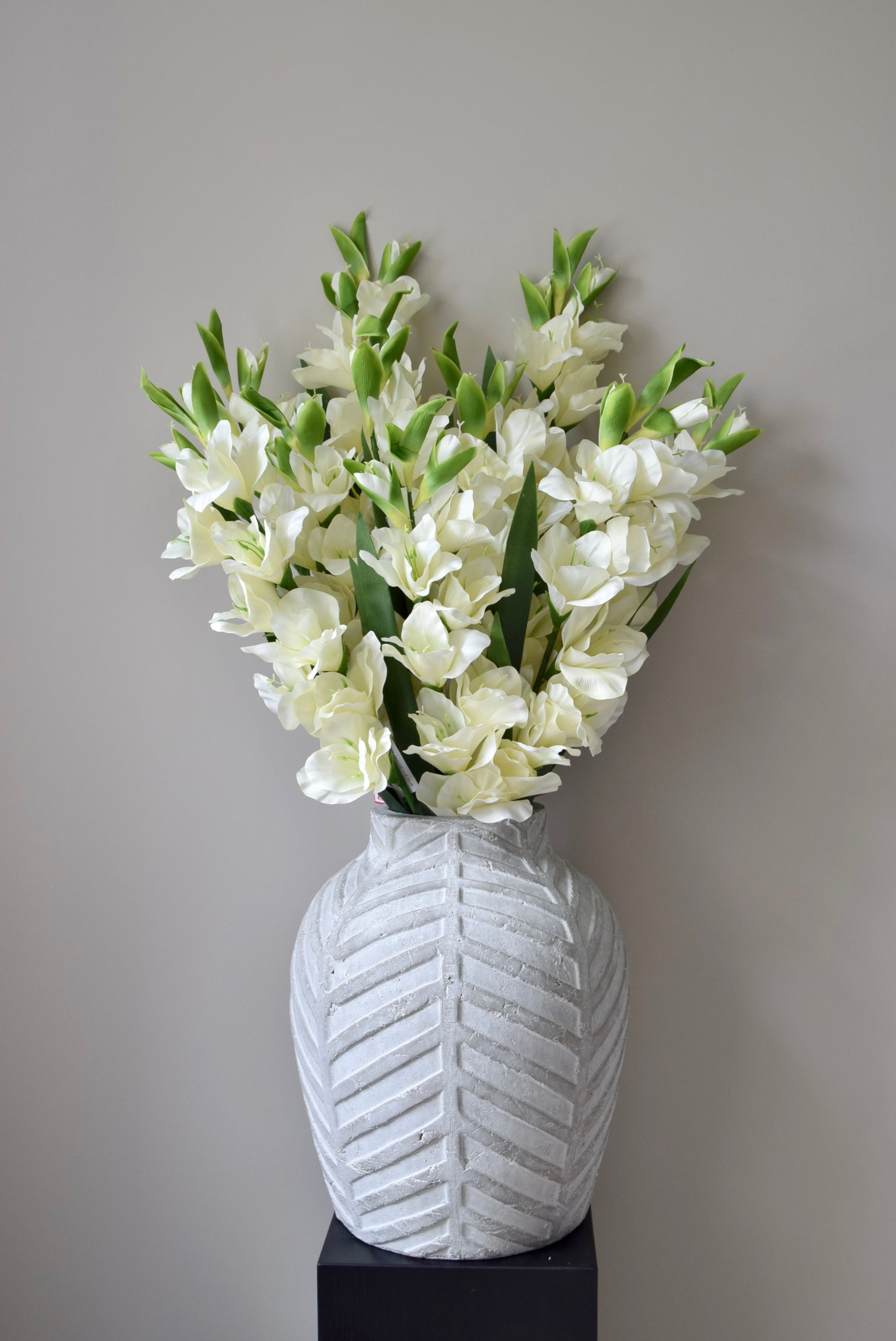 White flowers in a textured white vase against a gray background