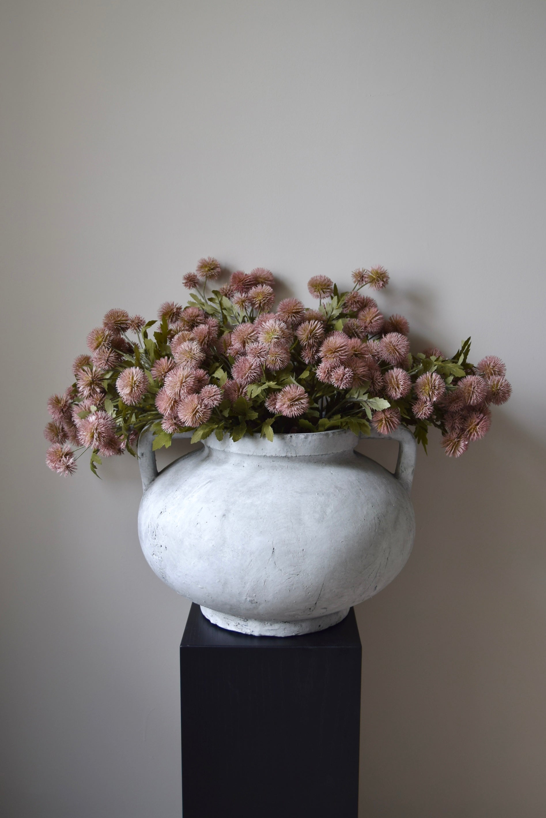 Decorative vase with pink flowers against a plain wall