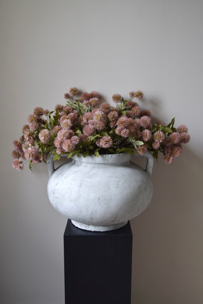 White vase with pink flowers on a black pedestal against a plain background