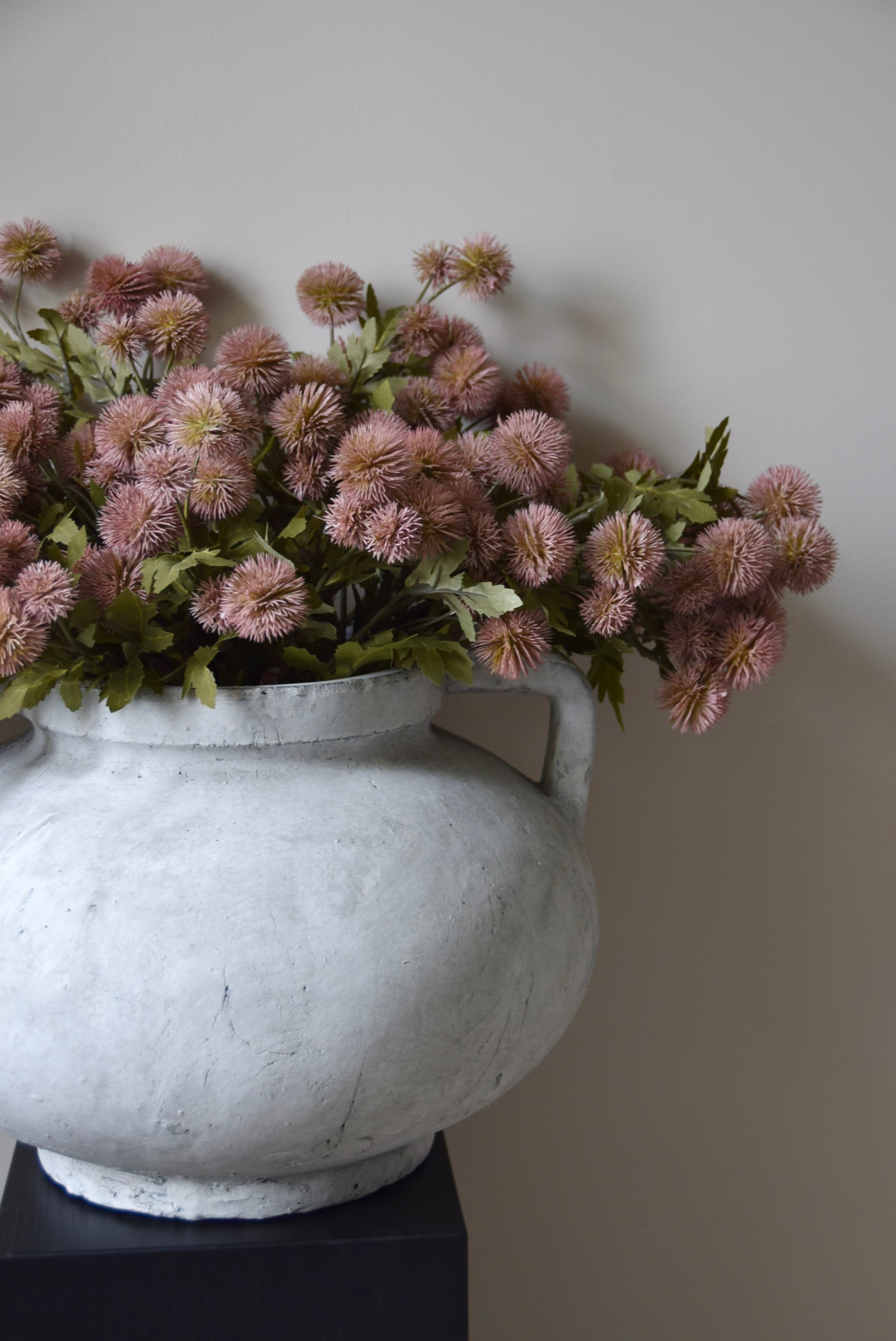 Decorative vase with pink flowers against a plain wall