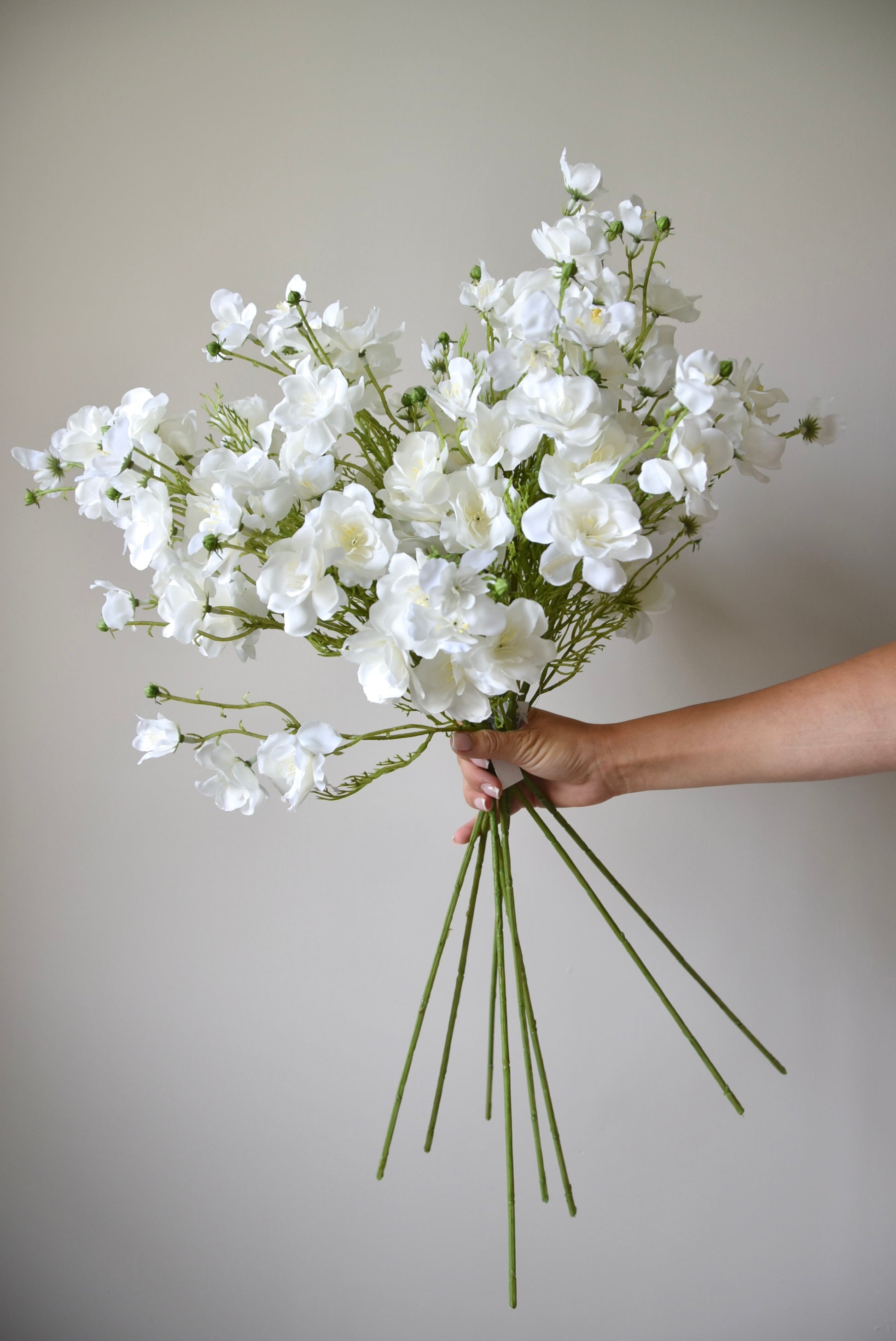 Bouquet of white flowers held by a person against a plain background
