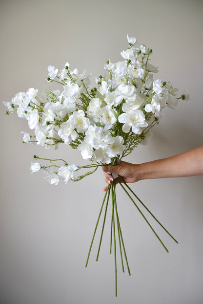 Bouquet of white flowers held by a person against a plain background