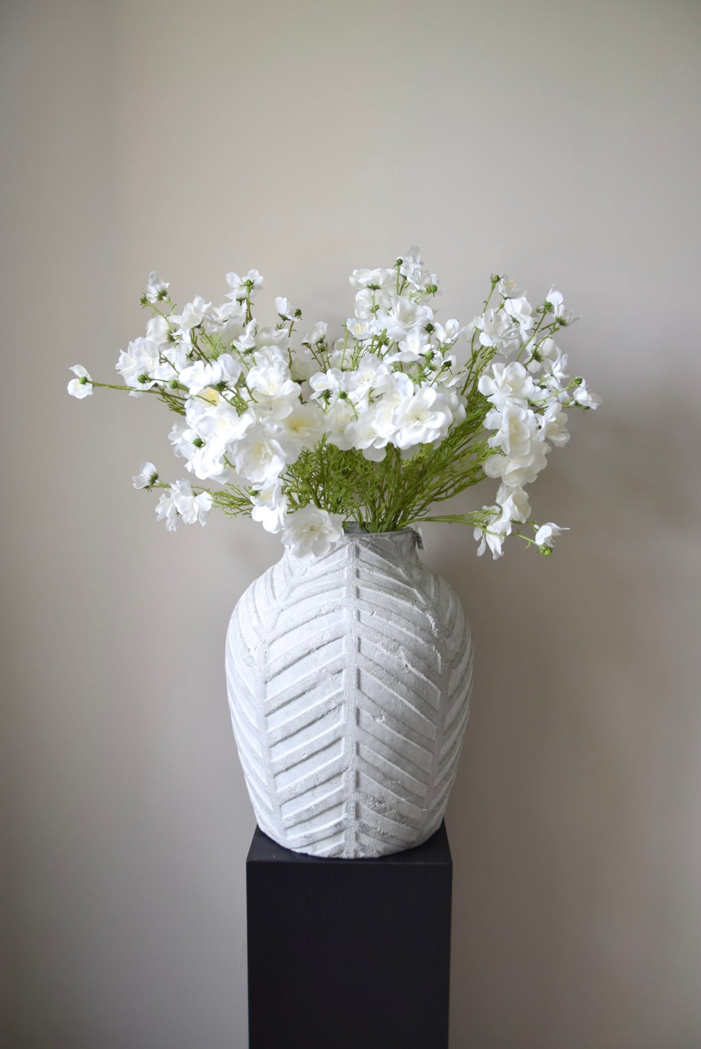 White textured vase with a bouquet of white flowers on a plain background