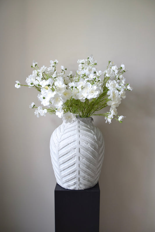 White textured vase with a bouquet of white flowers on a plain background