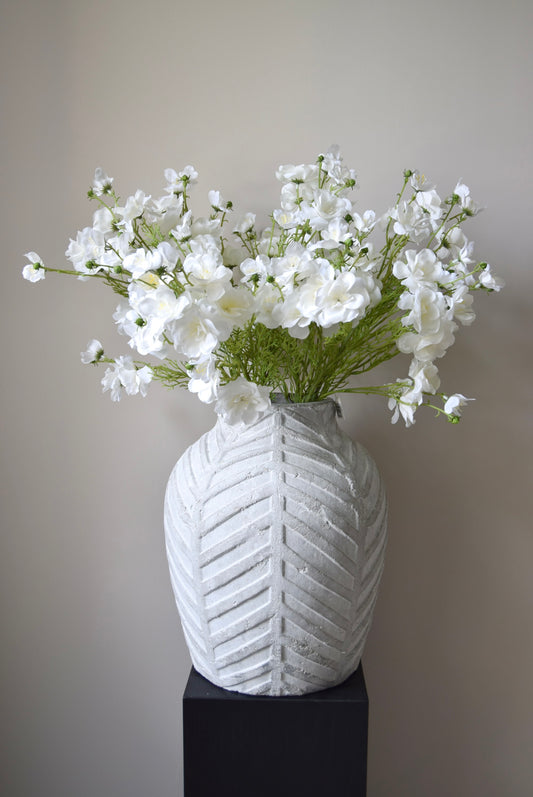 White textured vase with a bouquet of white flowers on a plain background