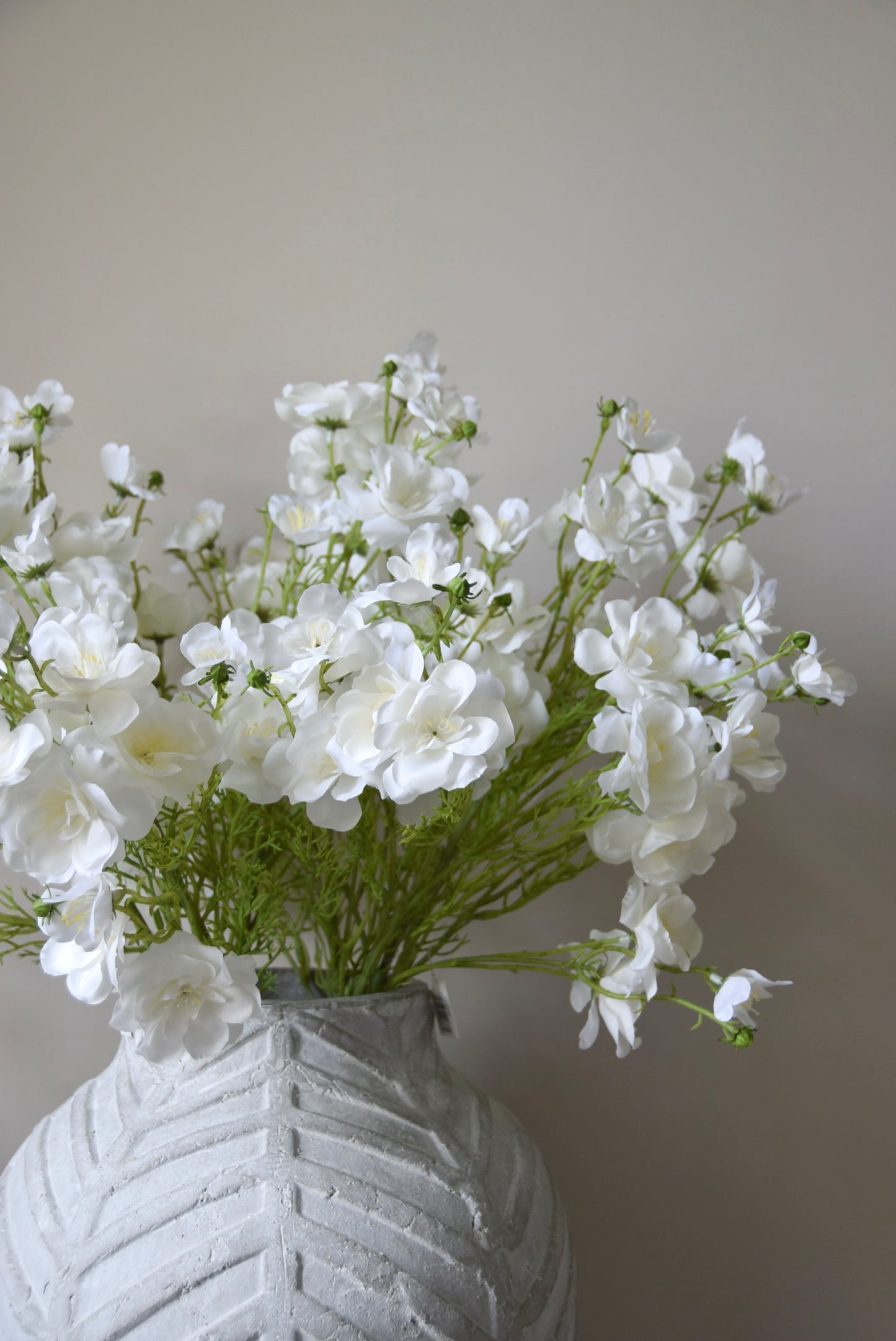 White flowers in a textured gray vase against a plain background