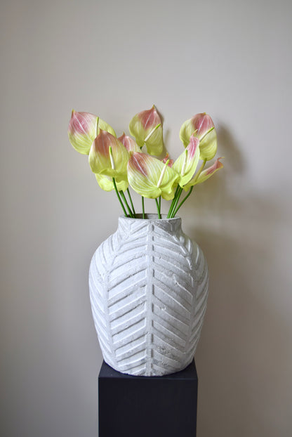 White textured vase with green and pink flowers on a plain background