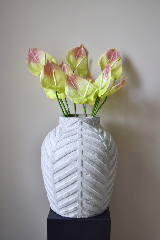 White textured vase with chevron pattern holding pink and yellow flowers against a plain background