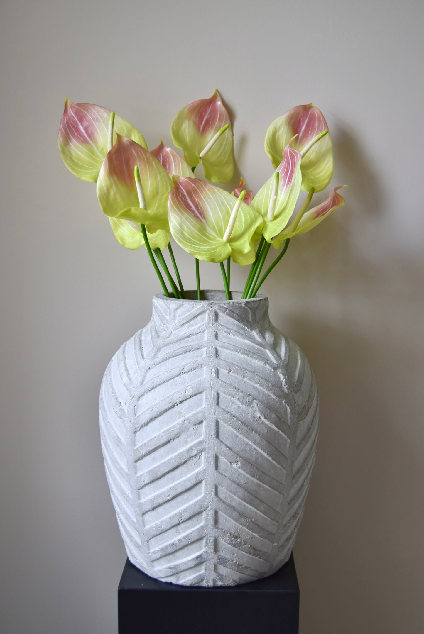 White textured vase with chevron pattern holding light pink and green flowers against a plain background