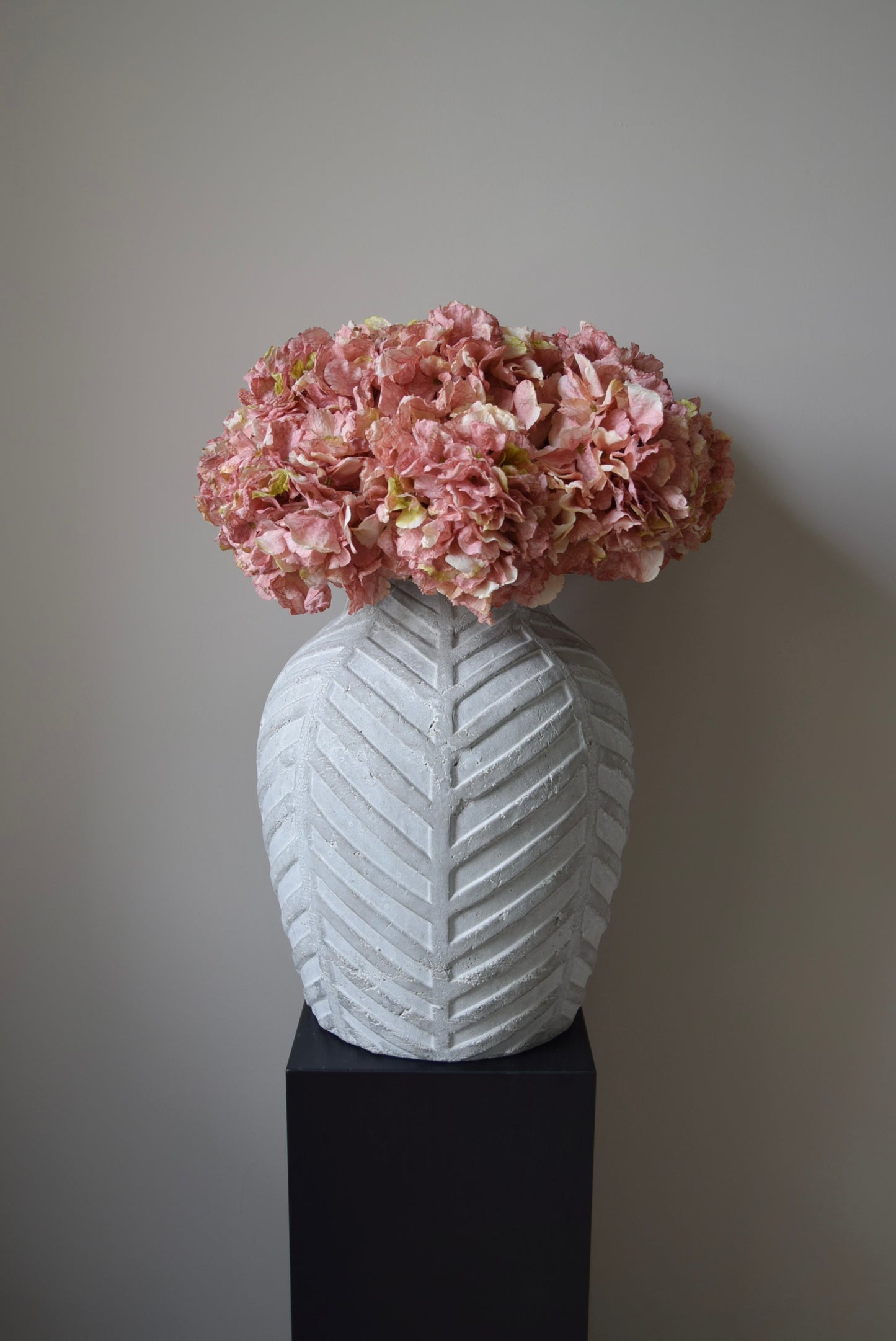 White textured vase with pink flowers against a plain background