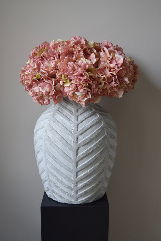 White textured vase with pink flowers against a plain background