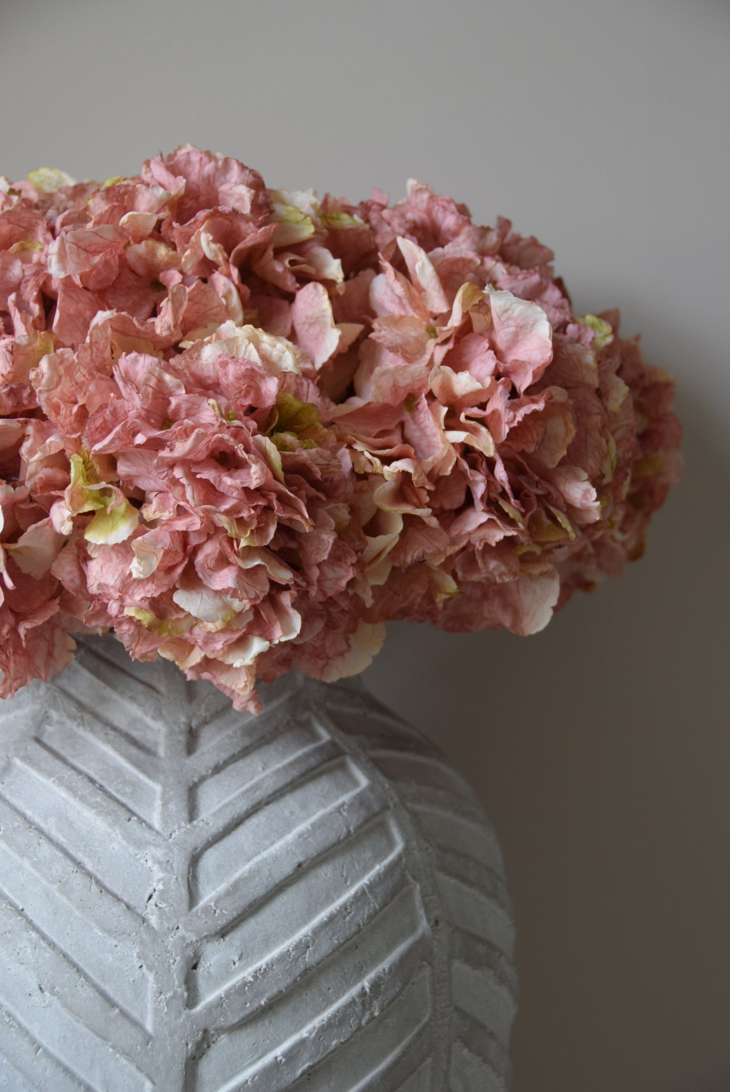 Pink hydrangea flower arrangement next to a textured gray vase on a light background