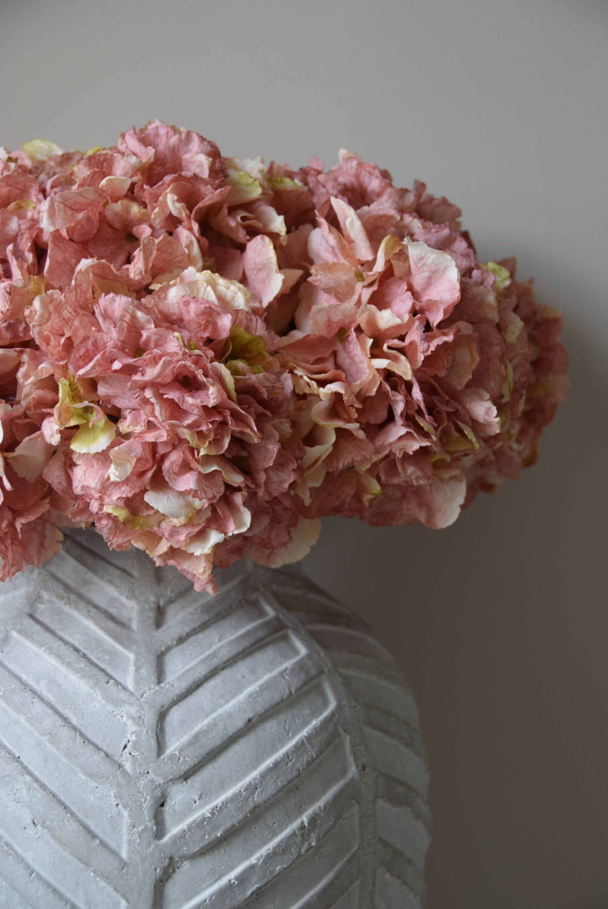 Pink hydrangea flower arrangement next to a textured gray vase on a light background