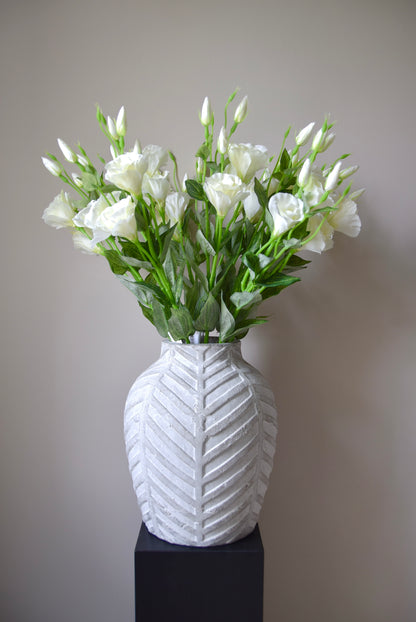 White vase with a textured pattern containing white flowers against a plain background