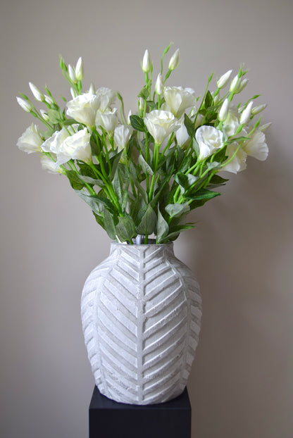White vase with a textured pattern containing a bouquet of white flowers on a plain background
