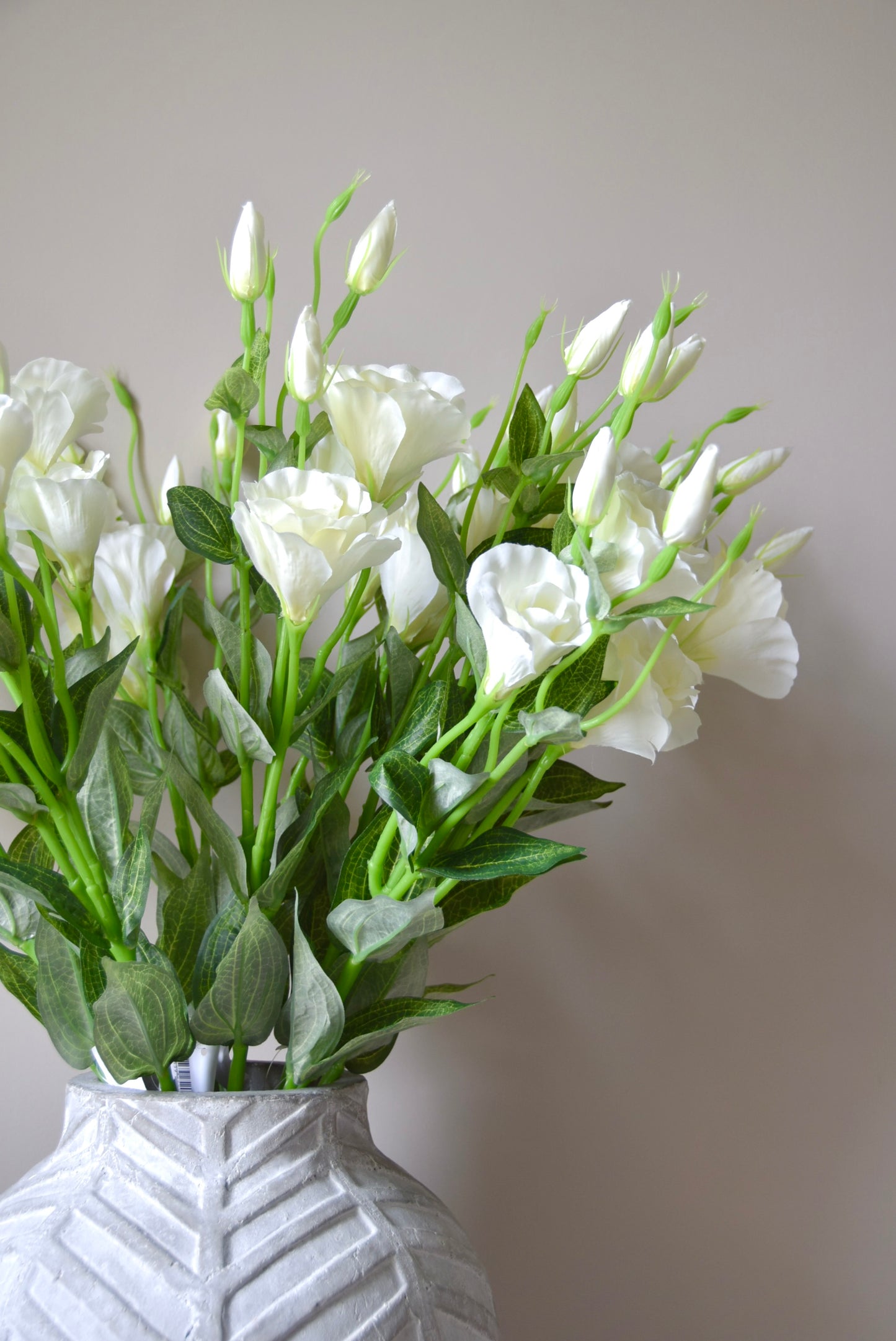 White flowers in a textured white vase against a plain background