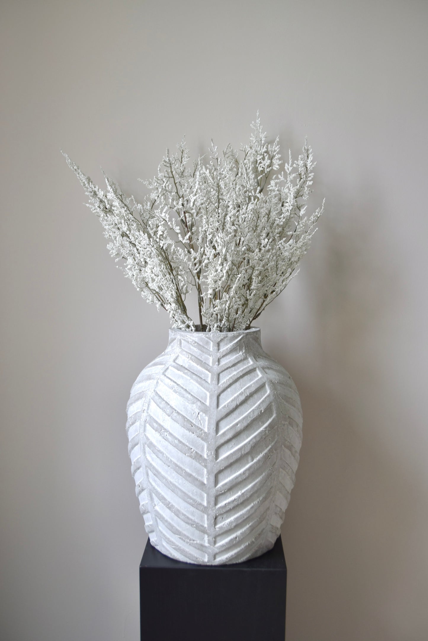White textured vase with dried white branches against a plain background