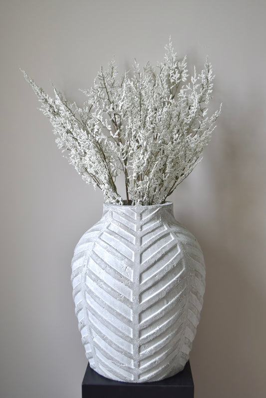 White textured vase with dried white flowers against a plain background